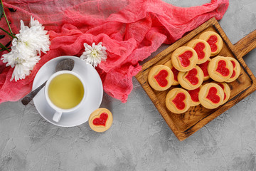 Flat lay. Cup with tea and cookies with a heart on a decorative board is an ornament of fresh flowers. Valentine's day concept.