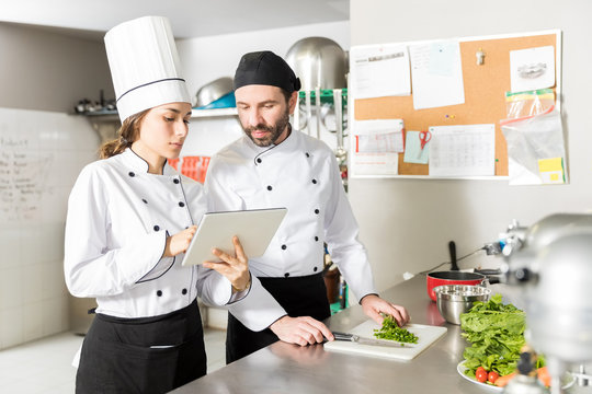Chefs Using Tablet Computer In Restaurant Kitchen