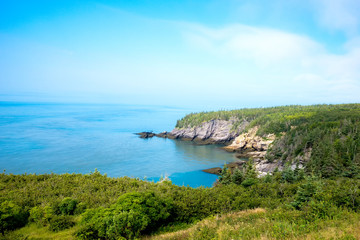 Naklejka na ściany i meble Scenic coastal view. Fog over the ocean in the distance. Blue ocean and sky. Trees and cliff. Taken at Cape Spencer, NB, Canada.