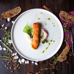 salmon on a pillow of mashed potatoes on a white plate on a dark wooden table next to the bread and table decorations