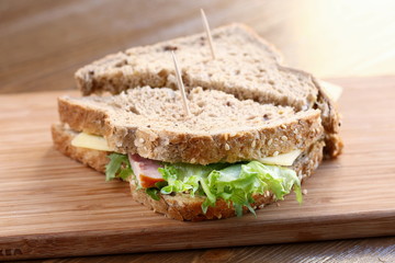 Delicious sandwich with natural green salad lettuce, cheese and ham, whole grain bread on a wooden plate board as a healthy snack for lunch