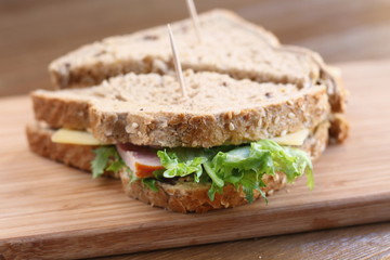 Delicious sandwich with natural green salad lettuce, cheese and ham, whole grain bread on a wooden plate board as a healthy snack for lunch