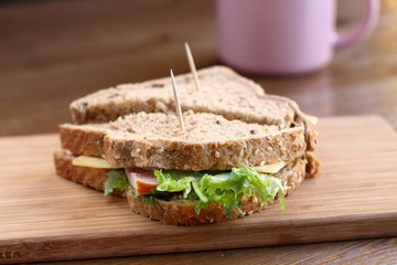 Delicious sandwich with natural green salad, cheese and ham, whole wheat bread on a wooden plate board as a healthy snack for lunch with pink mug on a background