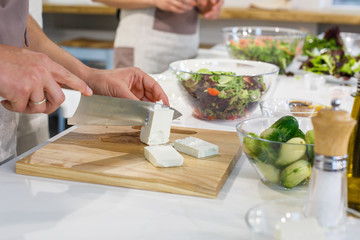 Chef cutting cheese Feta in white kitchen. Family dinner on holidays. Cooking in cozy cuisine at home