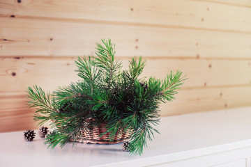 Green pine branches in a wicker basket on a white chest of drawers on a wooden background