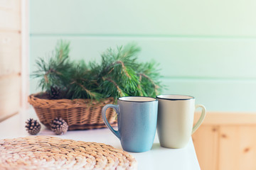 Morning interior. Two cups with a drink and a bouquet of pine needles on a white table in the morning Sunny day.