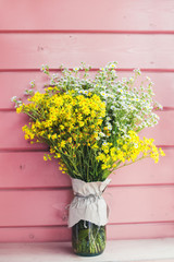 Home decor. Wildflowers in a vase on a background of wooden pink boards.	