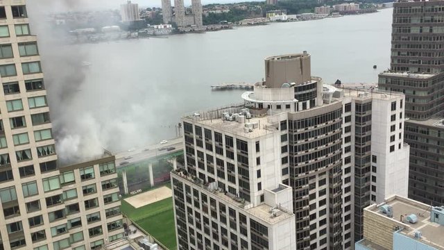 New York City firefighters respond to fire on top of section of building in Manhattan.  Fireman put out apartment fire on roof of building as smoke rises from flames.