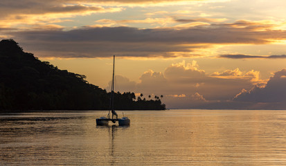 Lonely catamaran against the background a golden sunset near Bora-Bora island in the Pacific ocean, French Polynesia. - obrazy, fototapety, plakaty
