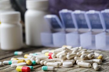 Variety of pills in white plastic pill organizer on weathered wood