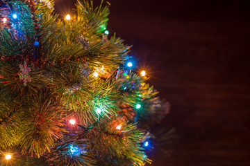 Christmas tree part with snowflakes and  garland with aquamarine, blue, pink and yellow lights on the left side of the frame and brown background