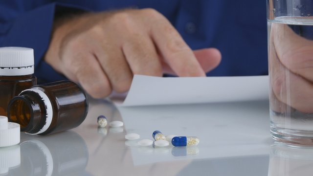 Suffering Man Reading and Checking a Medical Prescript with Pills on the Table
