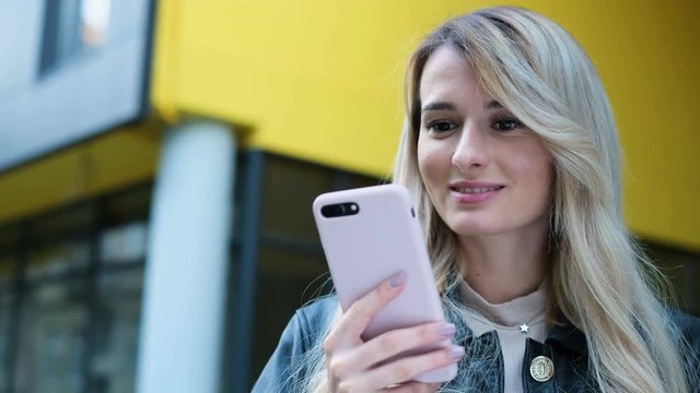 Close-up portrait of woman in the city uses smartphone outdoor. Pretty hipster, student girl texting and using app on smart phone on yellow background. Lifestyle, urban