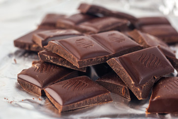 Several pieces of chocolate of the variety bittersweet lie on a silver paper