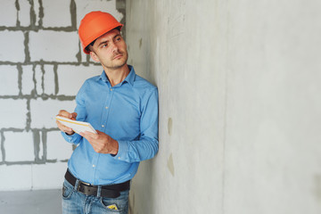 Construction supervisor writes on notebook near the wall. Handsome foreman taking notes in...