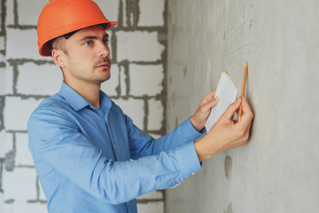Construction supervisor writes on notebook near the wall. Handsome foreman taking notes in...