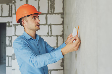 Construction supervisor writes on notebook near the wall. Handsome foreman taking notes in...