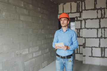 Construction supervisor writes on notebook near the wall. Handsome foreman taking notes in...