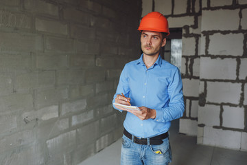 Construction supervisor writes on notebook near the wall. Handsome foreman taking notes in...