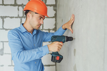 building, working equipment concept - builder in hardhat perforating wall with drill indoors