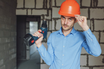 Smiling man with electric drill wearing protective helmet. Repair concept