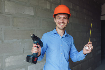 Smiling man with electric drill wearing protective helmet. Repair concept