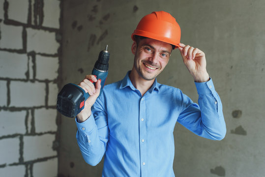 Smiling man with electric drill wearing protective helmet. Repair concept