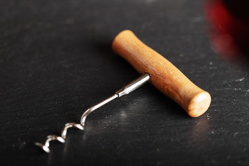 Corkscrew opener for wine cork on dark  wooden background. Bottle-screw to open wine alcohol bottle at rustic vintage black table.