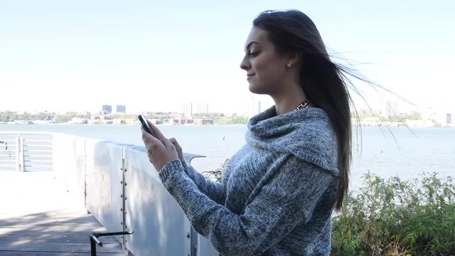 Young millennial beautiful happy busy woman girl outside walking and texting on cellphone mobile smartphone sending messages on social media and updating newsfeed on mobile device