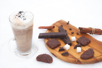 Glass of hot chocolate, cinnamon sticks, cookies and chocolate on snow. Winter refreshment.