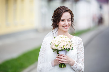 young beautiful bride girl with wedding bouquet of roses stands on the street. the wind blows the...