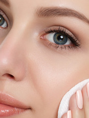 Fototapeta premium Portrait of young beautiful woman with towel on her hair cleaning makeup from her face with cosmetic pad isolated over white background. Cleaning face, perfect skin, skincare and cosmetology concept