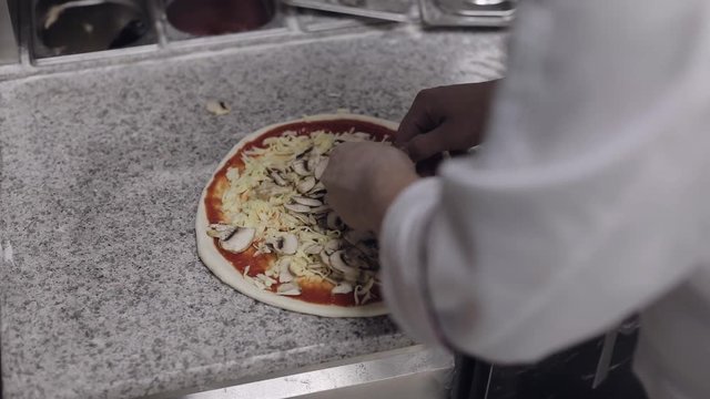 The chef cooks pizza. Puts the mushrooms on the dough which is anointed with tomato paste and covered with cheese