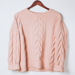 Female woolen sweater on hanger at white wall.