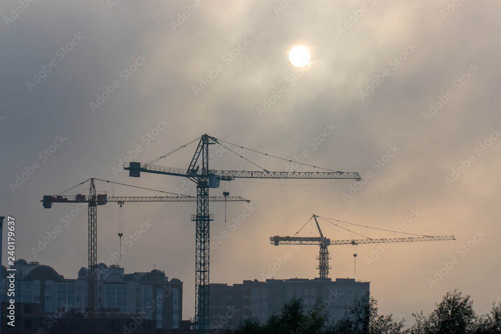 Wall mural very high construction crane in the morning fog, against the gray sky background