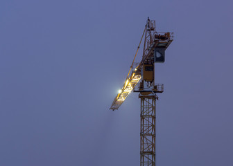 very high construction crane in the morning fog, against the gray sky background