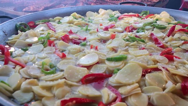 Cocinando en una sart&eacute;n gigante con aceite hirviendo un plato  realizado con patatas cortadas en rodajas , cebolla, pimientos de Padr&oacute;n, jamon y huevos ( Patatas a lo pobre )