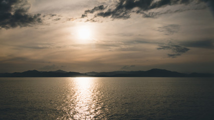 Golden sunset over the island of Jamaica. Mountains on the horizon in silhouette and sunlight reflected on the surface of the calm sea. Peaceful tropical evening scene.