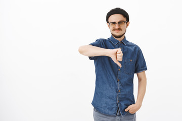 Studio shot of unsure dissatisfied cute young male student in black beanie and glasses smirking and...