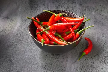 Keuken spatwand met foto Closeup on red hot chili peppers in ceramic bowl over dark textured table © tilialucida