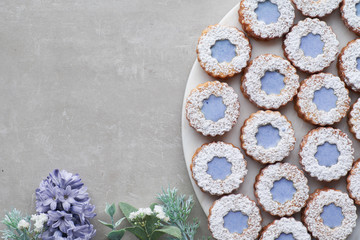 Flower Linzer cookies with blue glazing on light concrete decorated with blue hyacinth flowers, fir twigs and herbs