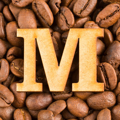M, Letter of the alphabet on wood- background of coffee beans.