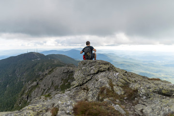 a hiker starts to take off his backpack while atop a mountain top