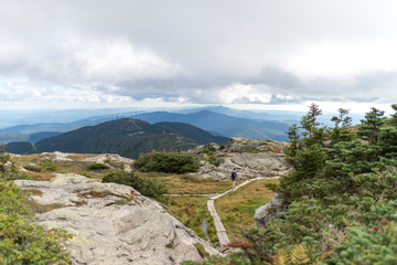 female hiker with backpack follows a path along the highest peak in Vermont