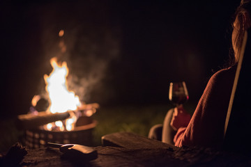 A women with a glass of wine looks at an outside fire