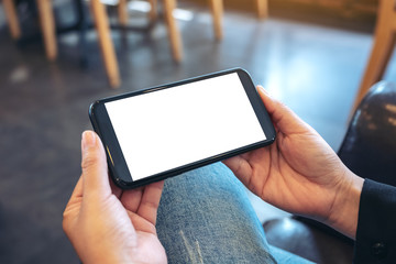 Mockup image of hands holding black mobile phone with blank white screen  horizontally in vintage...