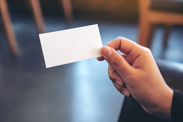 A hand holding white empty business card with blurred background