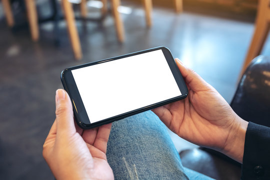 Mockup image of hands holding black mobile phone with blank white screen  horizontally in vintage cafe