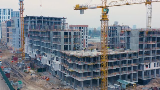 Aerial side view of a big construction site with an apartment houses in a course of building with a lot of builders in bright vests
