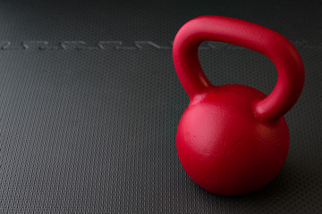 Naklejka na ściany i meble Red kettlebell on a black gym floor, simple commitment to fitness